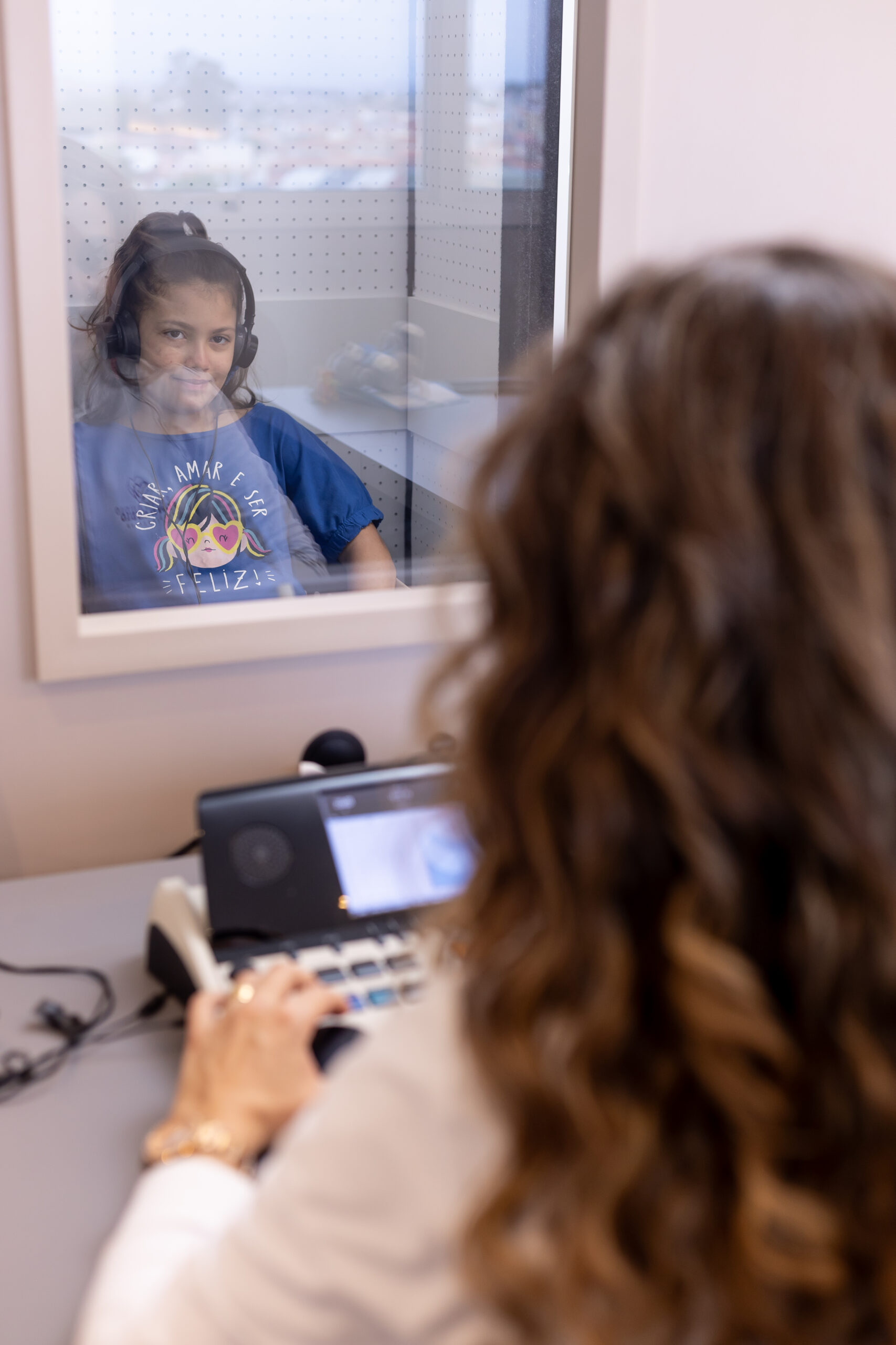 Criança na cabine de audiometria infantil em Indaiatuba, com a audiologista no audiômetro