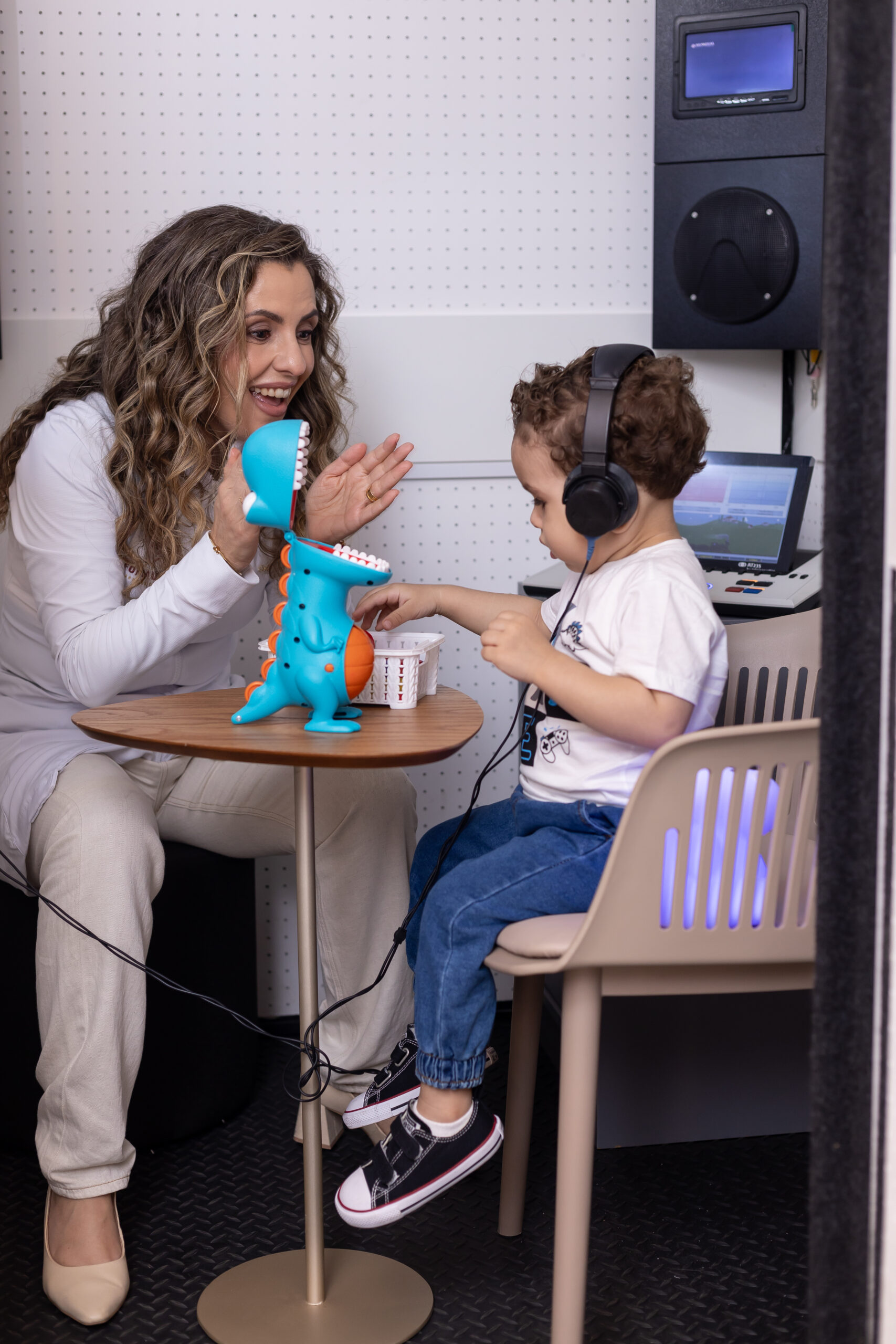 Audiometria infantil lúdica em Indaiatuba: Dra. Janaína Colon com uma criança de fone na cabine